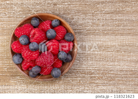 Mix of blueberries and raspberries in wooden plate on a rustic table. 118321623