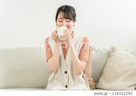 お茶・コーヒー・紅茶・ホットドリンクを飲んで休憩する・くつろぐソファに座る笑顔のアジア人女性 お茶・コーヒー・紅茶・ホットドリンクを飲んで休憩する・くつろぐソファに座る笑顔のアジア人女性 118322293