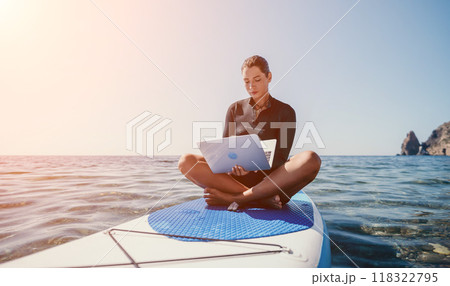 Digital nomad, freelancer, laptop. Happy smiling woman working on sup board at calm sea beach, relieves stress from work. Freelance, remote work on vacation, travel and holidays concept. Digital nomad, freelancer, laptop. Happy smiling woman working on sup board at calm sea beach, relieves stress from work. Freelance, remote work on vacation, travel and holidays concept. 118322795
