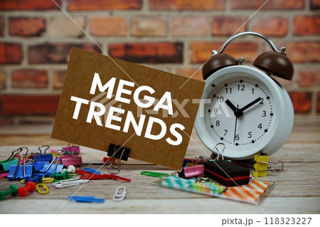Mega Trends text on paper card with alarm clock and stationary on wooden background Mega Trends text on paper card with alarm clock and stationary on wooden background 118323227