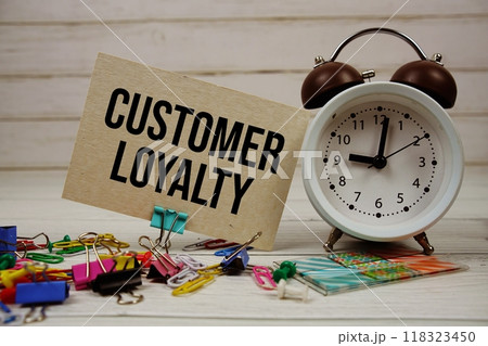 Customer Loyalty text on paper card with alarm clock and stationary on wooden background Customer Loyalty text on paper card with alarm clock and stationary on wooden background 118323450