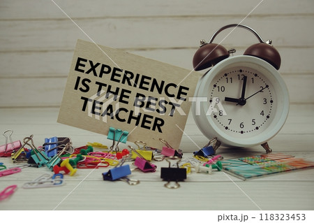 Experience is The Best Teacher text on paper card with alarm clock and stationary on wooden background 118323453