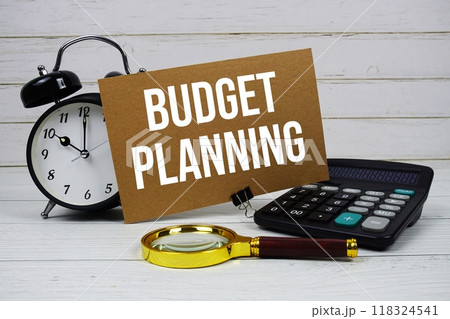 Budget Planning text on paper card with alarm clock, calculator and magnifying glass on wooden background Budget Planning text on paper card with alarm clock, calculator and magnifying glass on wooden background 118324541