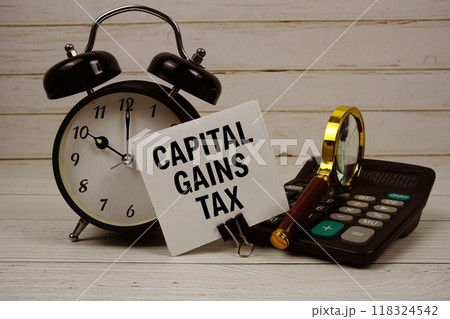 Capital Gains Tax text on paper card with alarm clock, calculator and magnifying glass on wooden background Capital Gains Tax text on paper card with alarm clock, calculator and magnifying glass on wooden background 118324542