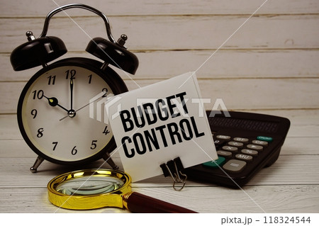 Budget Control text on paper card with alarm clock, calculator and magnifying glass on wooden background Budget Control text on paper card with alarm clock, calculator and magnifying glass on wooden background 118324544