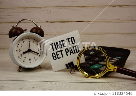 Time to Get Paid text on paper card with alarm clock, calculator and magnifying glass on wooden background Time to Get Paid text on paper card with alarm clock, calculator and magnifying glass on wooden background 118324546