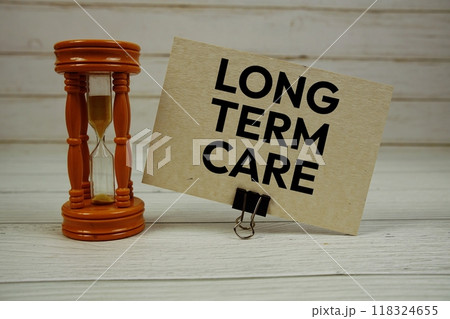 Long Term Care text on paper card with Hourglass on wooden background 118324655