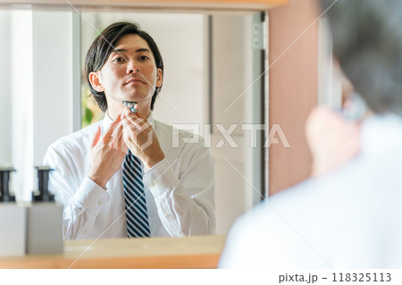 朝出勤前に洗面所で髭剃りをするスーツ姿の若いアジア人ビジネスマン 118325113