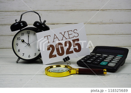 Taxes 2025 text on paper card with alarm clock, calculator and magnifying glass on wooden background Taxes 2025 text on paper card with alarm clock, calculator and magnifying glass on wooden background 118325689