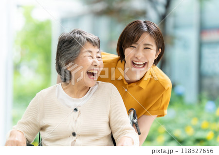 車椅子のシニア女性と介護する若い女性 車椅子のシニア女性と介護する若い女性 118327656