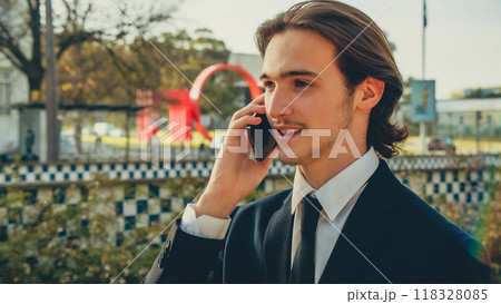 Smiling businessman in the city talking on a cell phone. Portrait Businessman in a business suit in the the street a with mobile phone. Young man in a business  suit talking on a smartphone. 118328085