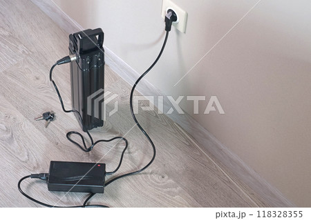 Charging bicycle battery from mains electricity in house. Socket in room with plug switched on. Environmentally friendly transport.  118328355