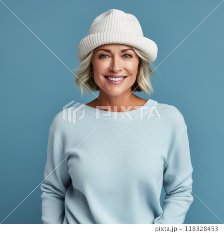 Happy middle aged woman in a beige winter hat and a blue sweater. Portrait of beautiful mature woman in a winter cap smiling on a blue background looking at camera. Cheerful caucasian woman in a hat. 118328453