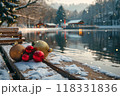 Snow-Covered Bench with Christmas Ornaments at Sunset Over a Mountain Lake in a Winter Holiday Village 118331836