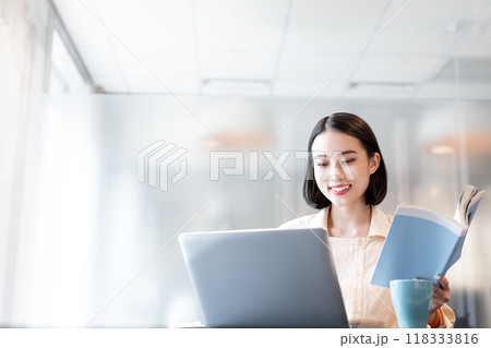 本を片手に笑顔でパソコンを操作する女性 本を片手に笑顔でパソコンを操作する女性 118333816