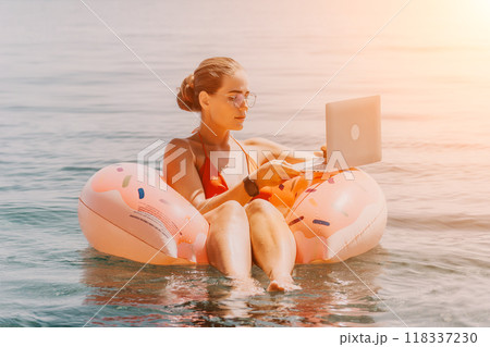 Woman Laptop Beach - Working on a laptop while floating on a flamingo pool float in the ocean on a sunny day. 118337230