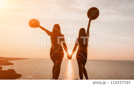Silhouettes of Two Women with Hats at Sunset Overlooking the Ocean 118337585