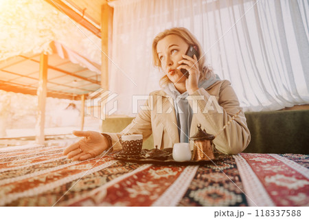 Woman Talking on Phone at a Cafe Table with Turkish Coffee Woman Talking on Phone at a Cafe Table with Turkish Coffee 118337588