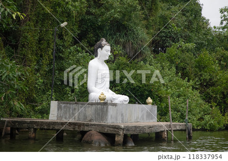 Beruwala,Sri Lanka. 02 february 2023 .white Buddha figure sits over lake. Background beautiful nature palm trees,blue sky. Asia travel and religion concept 118337954