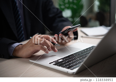 Hands of businessman using smartphone and laptop, indicating modern business communication and multitasking. Perfect for corporate environments, tech firms, productivity themes. 118338951