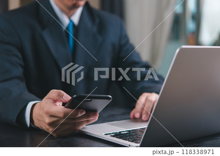 Businessman using phone and laptop simultaneously. Concept of multitasking, modern work environment, professional communication. Ideal for corporate, business settings. Businessman using phone and laptop simultaneously. Concept of multitasking, modern work environment, professional communication. Ideal for corporate, business settings. 118338971