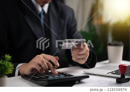 Businessman using calculator and holding credit card. Concept of finance, accounting, payment calculation. Suitable for financial services, business management. Businessman using calculator and holding credit card. Concept of finance, accounting, payment calculation. Suitable for financial services, business management. 118338974
