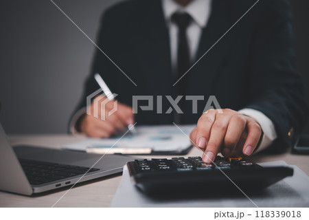 Close-up of a businessman in a suit working at a desk. Hand pressing calculator, analyzing documents. Professional, focused on financial calculations. Suitable for business, finance, 118339018