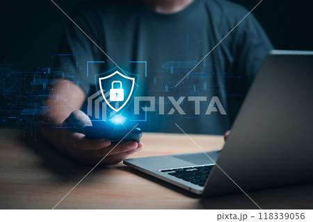 Hand holding smartphone with cybersecurity hologram, laptop in background. Represents data protection and digital security. Great for tech firms, cybersecurity awareness, and online privacy. 118339056