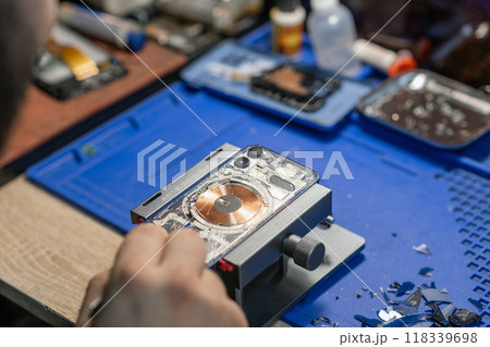 A technician carefully repairs a smartphone, focusing on battery replacement amidst various tools and parts in the workshop. A technician carefully repairs a smartphone, focusing on battery replacement amidst various tools and parts in the workshop. 118339698