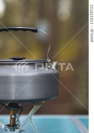 A kettle is heating up on a small camping stove as steam begins to rise in the cool forest air. A kettle is heating up on a small camping stove as steam begins to rise in the cool forest air. 118339722