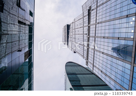 Modern Moscow City towers against a blue sky. Tall glass skyscrapers with mirrored facades reflect city lights and clouds, creating a dynamic urban landscape. 118339743