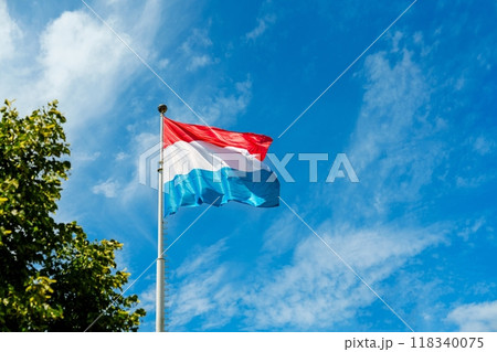 Flag of Luxembourg blowing in the wind against a blue sky with white clouds 118340075