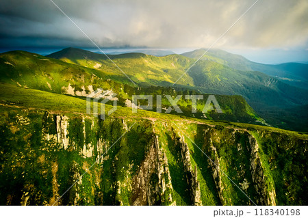 Breathtaking aerial view of green, rugged mountain peaks under dramatic sky. Scene captures contrast between vibrant landscape and moody clouds, with sunlight breaking through. Carpathians, Chornogora Breathtaking aerial view of green, rugged mountain peaks under dramatic sky. Scene captures contrast between vibrant landscape and moody clouds, with sunlight breaking through. Carpathians, Chornogora 118340198
