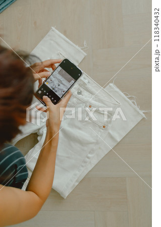 Woman taking photo of her white jeans while measuring for selling online. Woman taking photo of her white jeans while measuring for selling online. 118340432