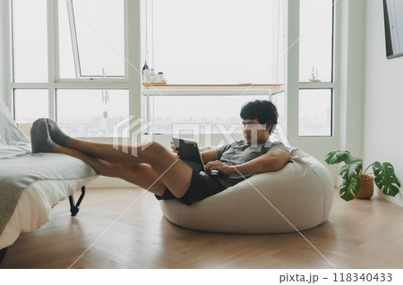 Man working with his laptop lying on the bean bag sofa in living room. Man working with his laptop lying on the bean bag sofa in living room. 118340433