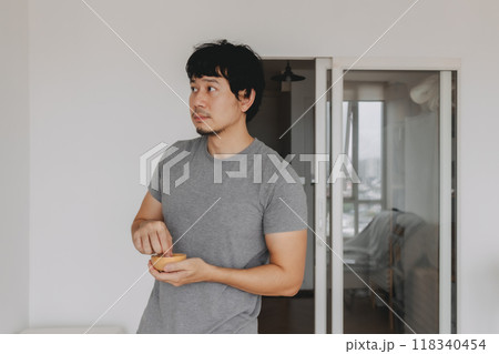 Man standing and eating peanuts snack while watching television in the room. 118340454