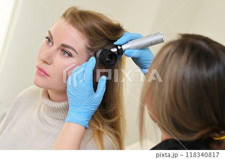 A dermatologist holds a dermatoscope in his hands and examines the structure of a young woman's hair. Trichoscopy is the science of hair structure. A dermatologist holds a dermatoscope in his hands and examines the structure of a young woman's hair. Trichoscopy is the science of hair structure. 118340817