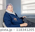 Elderly woman in a chair with a blank expression, typical of dementia, wrapped in a warm sweater. The image captures the solemn reality of living with severe cognitive decline. 118341205