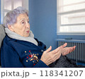 Elderly Alzheimer's patient in a nursing home setting, gesturing while talking to herself, highlighting the effects of senile dementia on communication and cognitive decline. 118341207