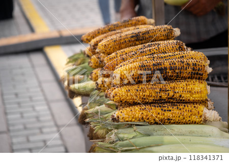 Freshly roasted corn on the cob is stacked neatly at a bustling outdoor market, enticing visitors with its smoky aroma. 118341371
