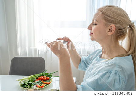 A woman is holding a smartphone and capturing a photo of a nutritious breakfast spread 118341402
