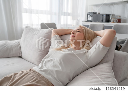 A woman relaxing on a sofa in a modern living room, enjoying a moment of calm and contentment 118341419