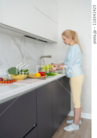 A woman is cleaning fresh vegetables in a modern kitchen to prepare a healthy meal 118341425