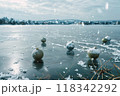 Winter Morning Scene with Christmas Decorations on a Snow-Dusted Frozen Lake in a Mountain Valley 118342292