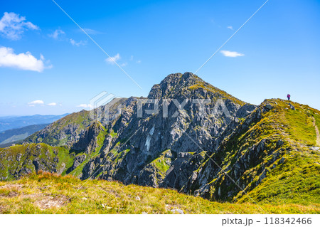 Under a clear blue sky, hikers explore the rugged terrain of Dumbier Mountain in the Low Tatras of Slovakia, surrounded by lush green hills and rocky peaks, enjoying the stunning panoramic views. Under a clear blue sky, hikers explore the rugged terrain of Dumbier Mountain in the Low Tatras of Slovakia, surrounded by lush green hills and rocky peaks, enjoying the stunning panoramic views. 118342466