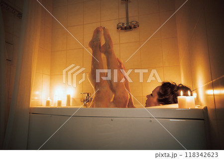 A woman is in a bathtub with candles lit around her. She is barefoot and has her legs up in the air. 118342623