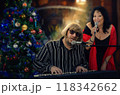 Christmas party comes alive with music - pianist and singer perform by brightly lit holiday tree. 118342662