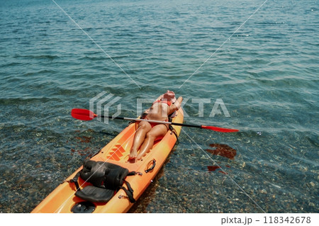 A woman is laying on a kayak in the water. The kayak is orange and has a paddle on it. The woman is wearing a red hat. A woman is laying on a kayak in the water. The kayak is orange and has a paddle on it. The woman is wearing a red hat. 118342678