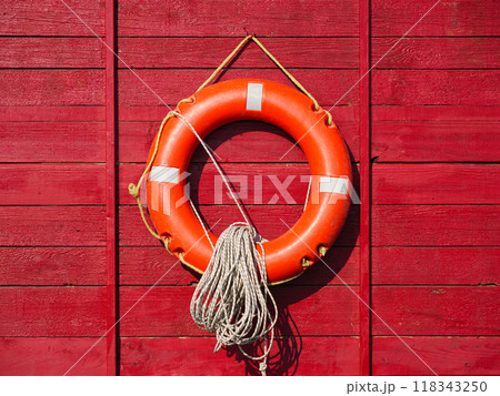 Bright orange life ring mounted on a red wooden wall with rope Bright orange life ring mounted on a red wooden wall with rope 118343250