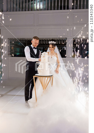 Enchanting Wedding Celebration - Bride and Groom Cutting Elegant Cake Amidst Sparkling Ambiance 118343340